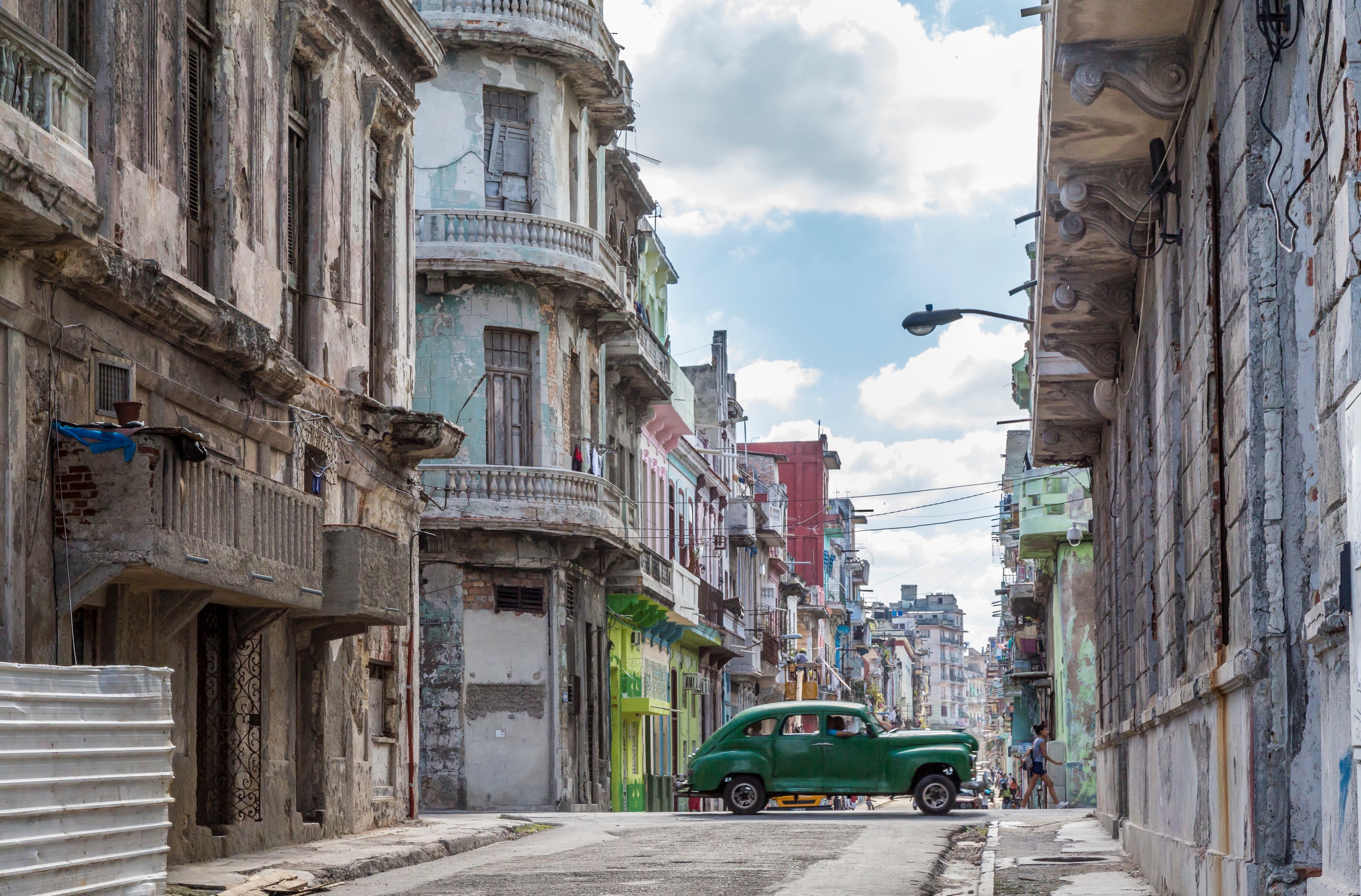 Gate med slitte, men fargerike hus i Cuba. Midt i gaten kjører en grønn bil.