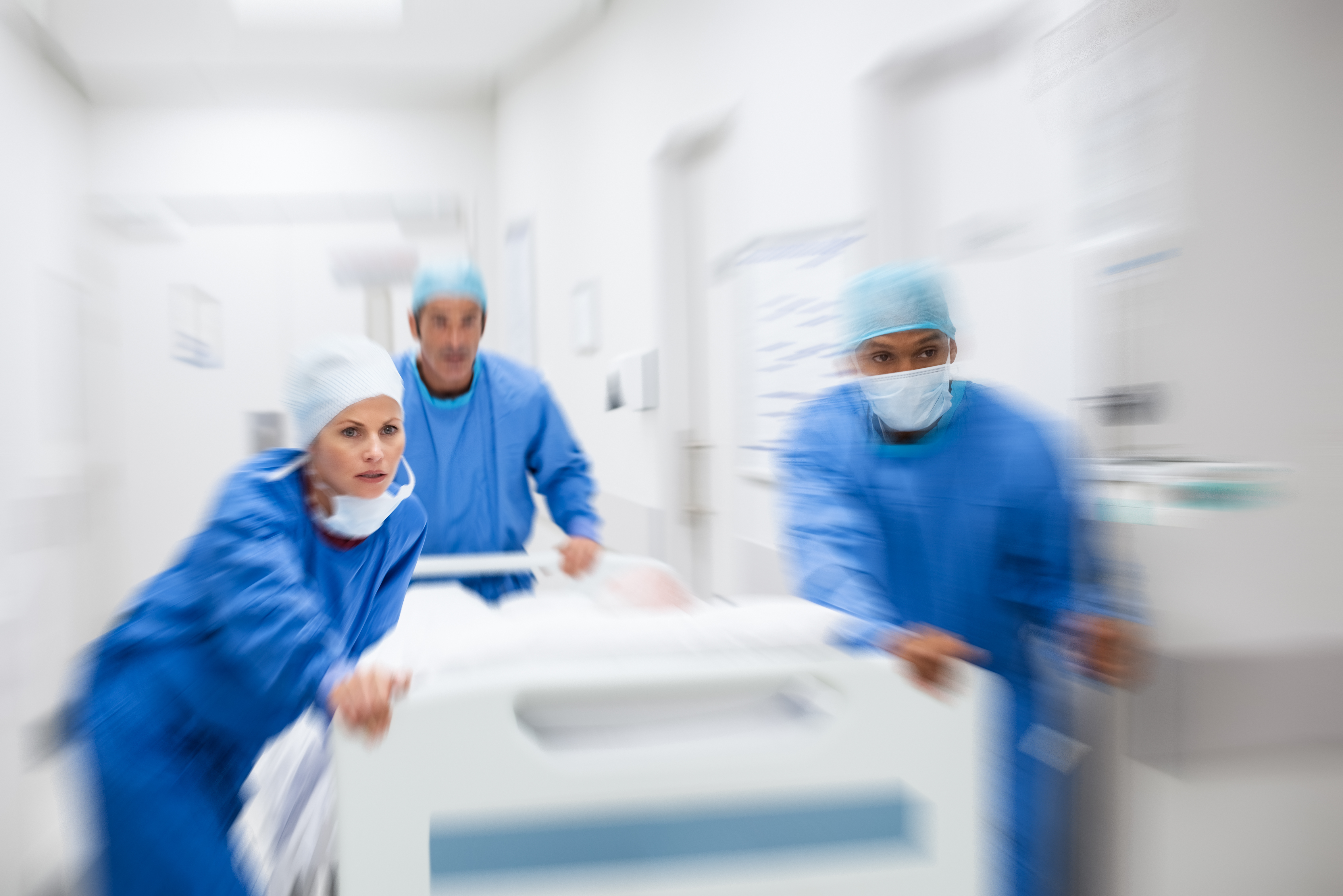 Tre helsepersonell i blå uniform transporter pasientseng til operasjonsstuen
