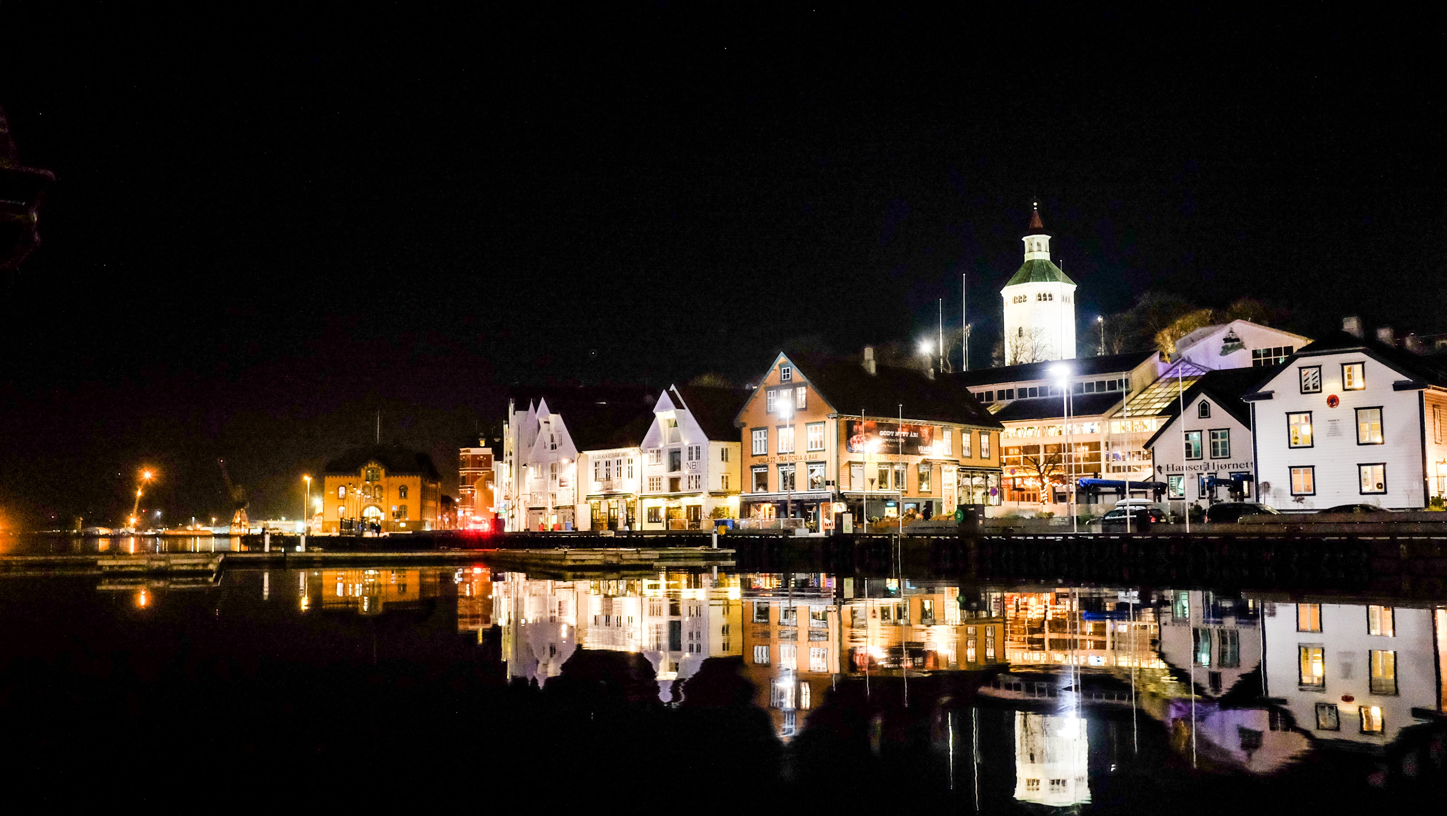 Bilde om natten av bygninger langs havnen i en by.