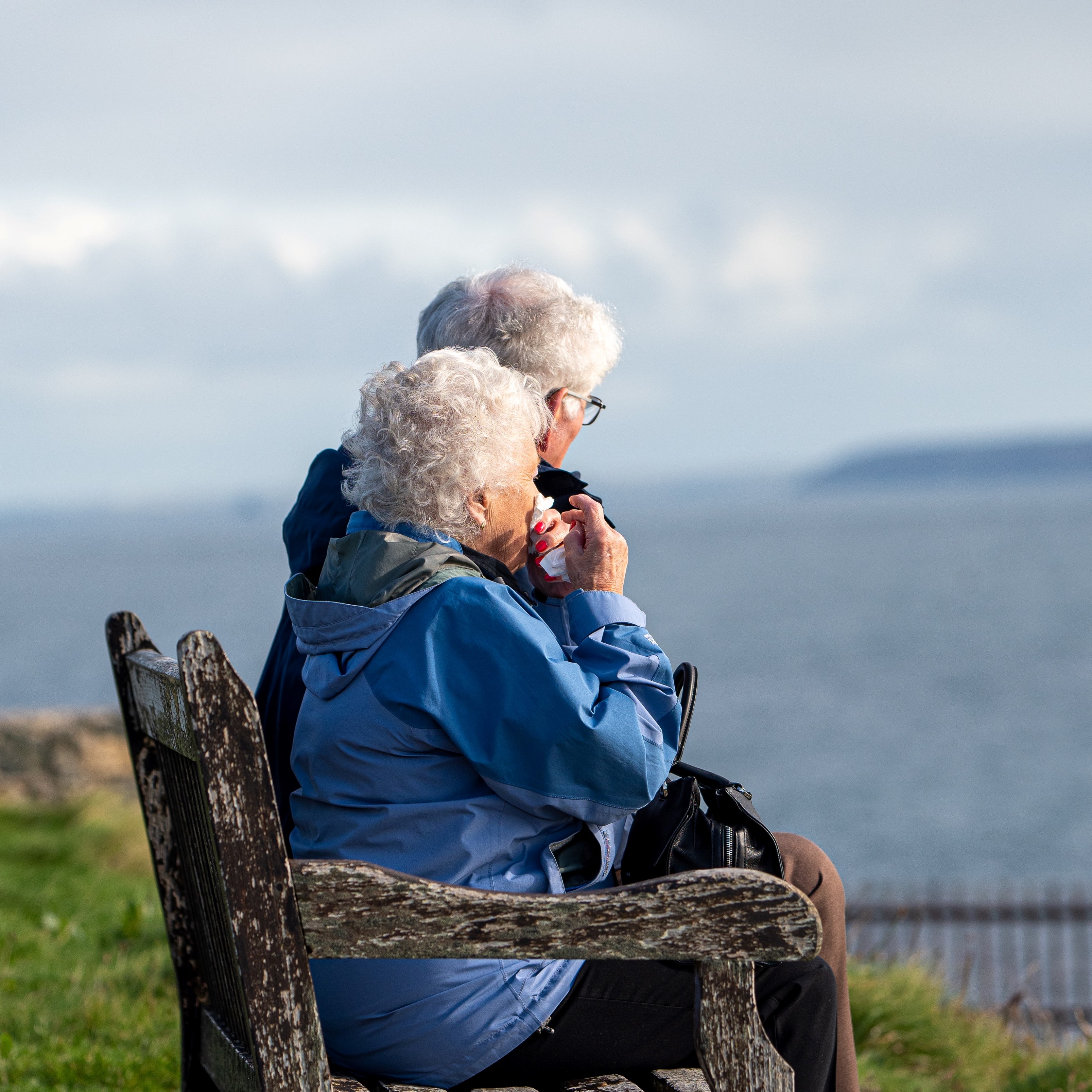 eldre par sitter på benk og ser utover sjøen, utsikt
