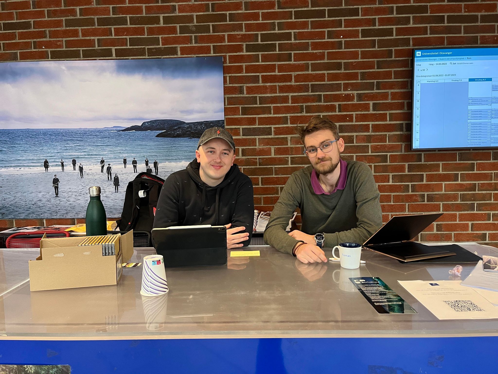 Kieran Sharkey og Tomas Carl Bruno Bjørn sitter på stand foran murveggen på campus Bjergsted