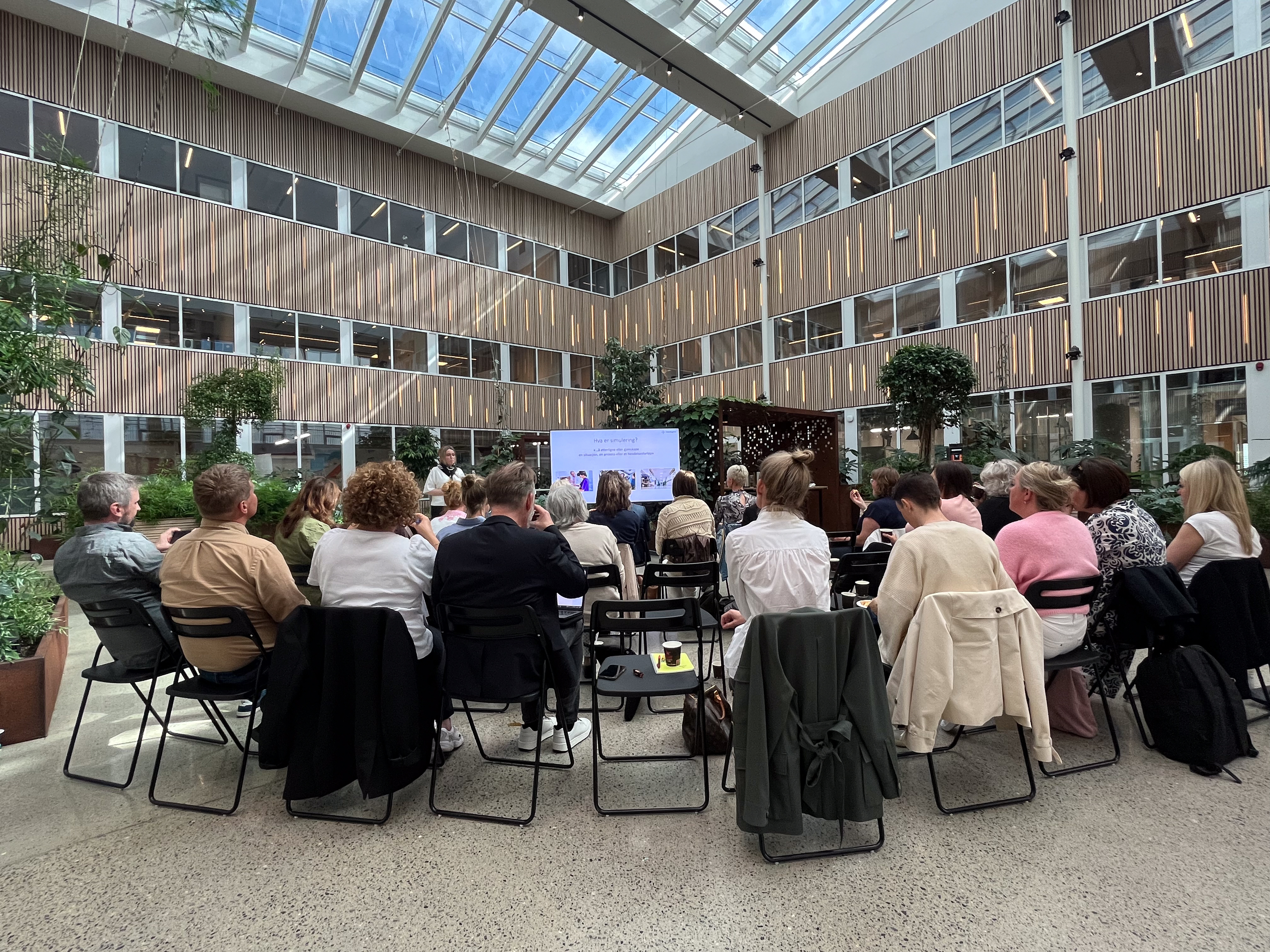 Mennesker som er samlet til seminar i et atrium