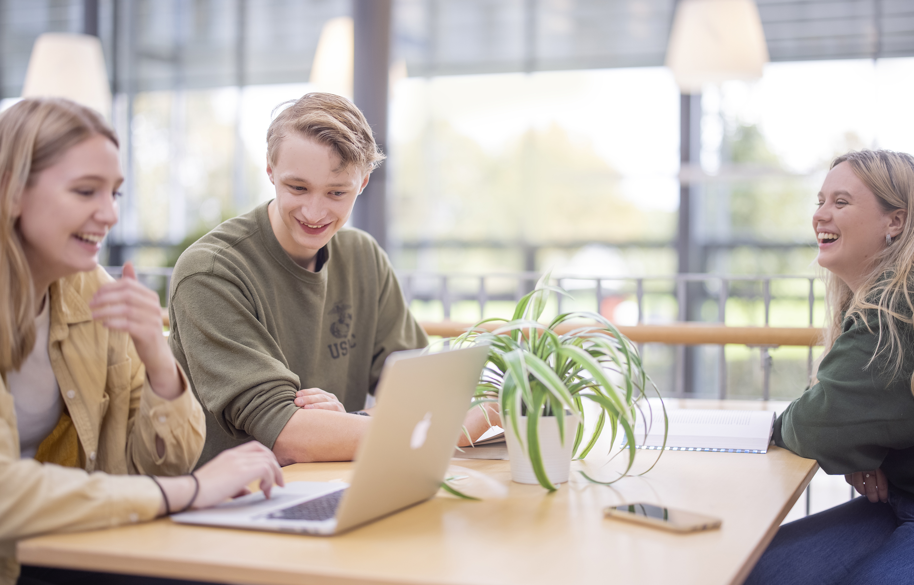 Tre studenter sitter rundt et bord og ser på en PC.