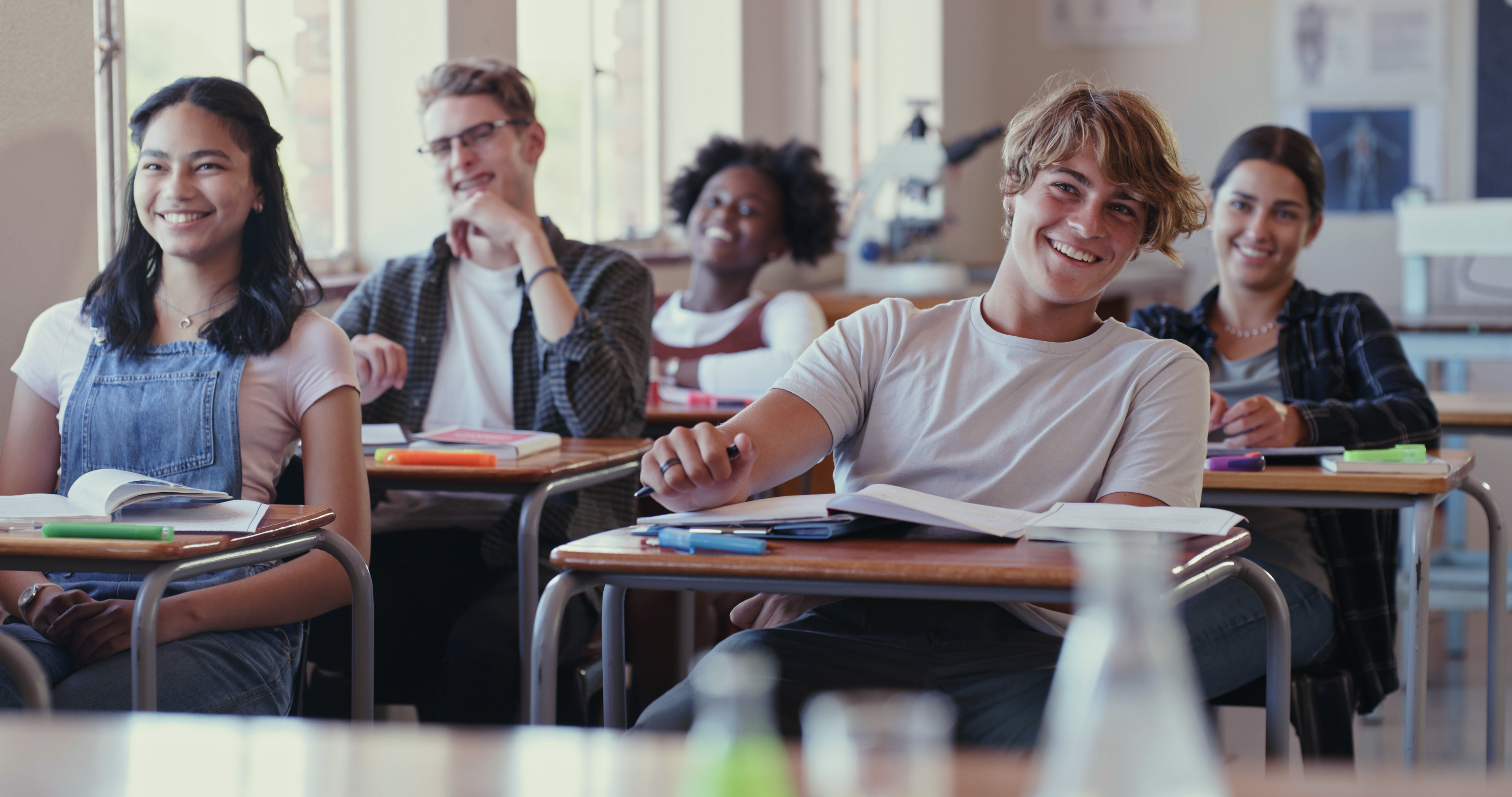 Ungdommer sitter ved pultene sine i et klasserom. De smiler mens det ser ut som om de ha undervisning