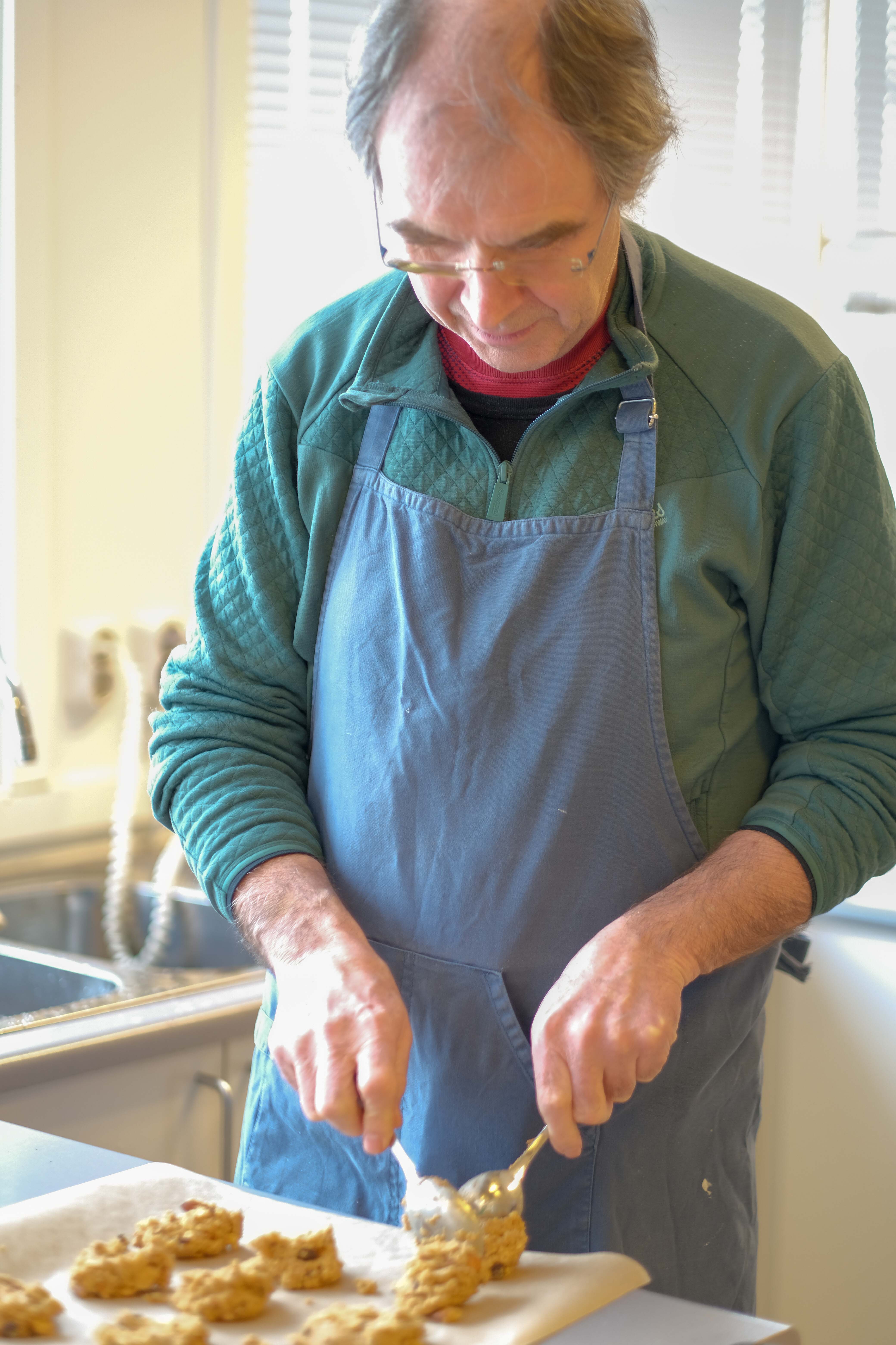 mann bruker to skjeer til å porsjonere og forme små deigtopper som han legger på bakepapir