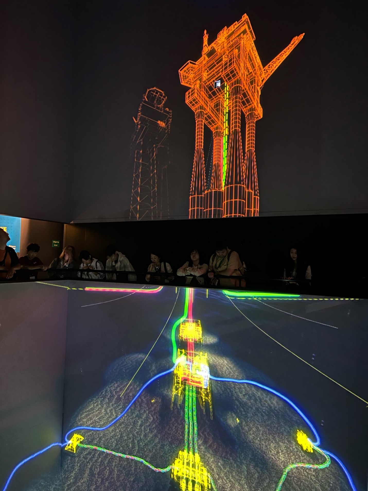 Audiovisual display of oil resources at the Norwegian Petroleum Museum. The image is a line drawing of an oil rig with a corrsponding image below showing connections between rigs and pipes