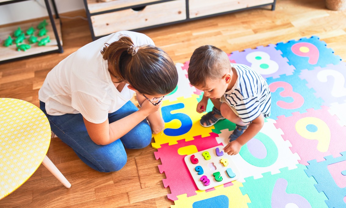 En liten gutt og en voksen kvinne leker med tall på gulvet