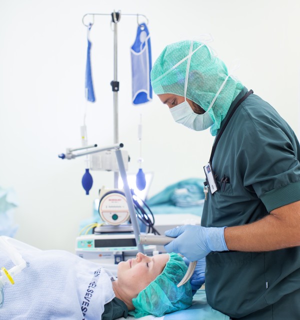 En mannlig anestesisykepleier i grønn uniform klargjør pasient på operasjonsbordet til intubering 