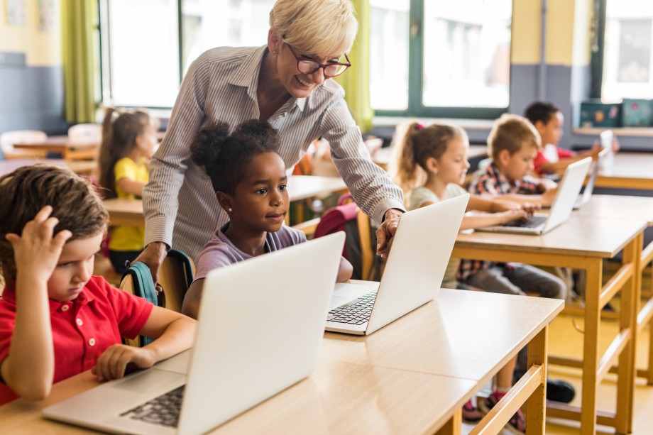 Lærer står over elever med pc-er i klasserom