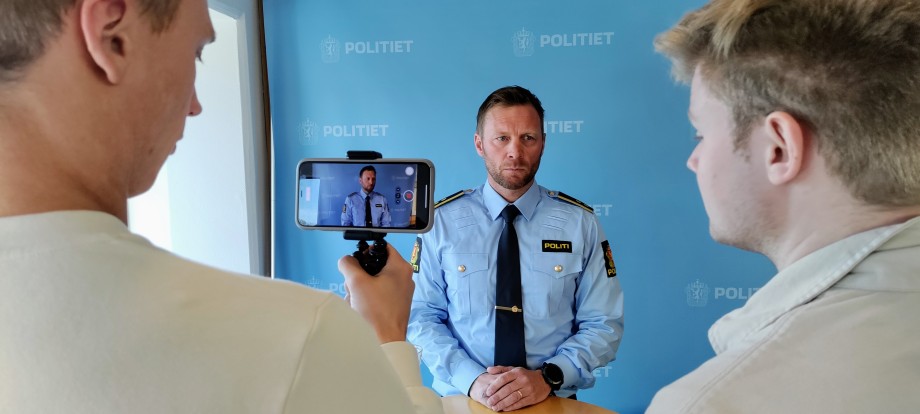 Politimann intervjues av studenter på en fiktiv pressekonferanse.