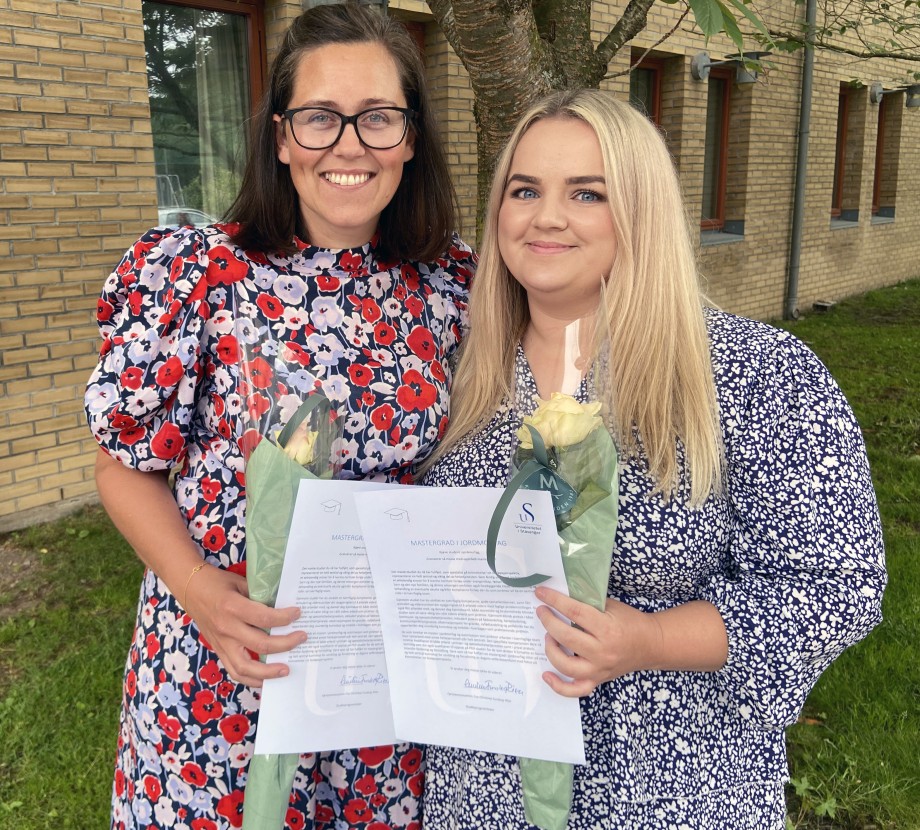 To kvinnelige studenter med fargerike kjoler og vitnemål