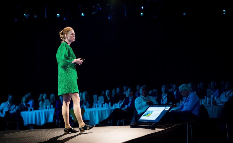 Professor Marte Solheim står på en scene og har presentasjon på Norway Summit foran publikum i sal