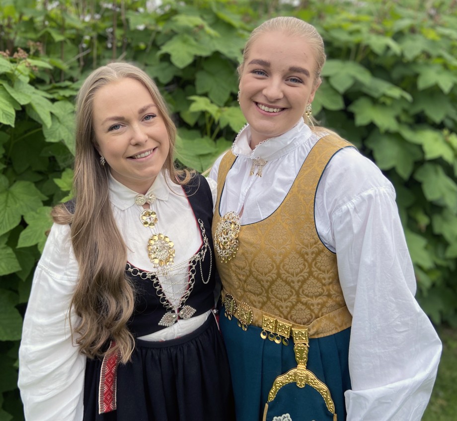 To kvinnelige studenter med bunad i naturlige omgivelser