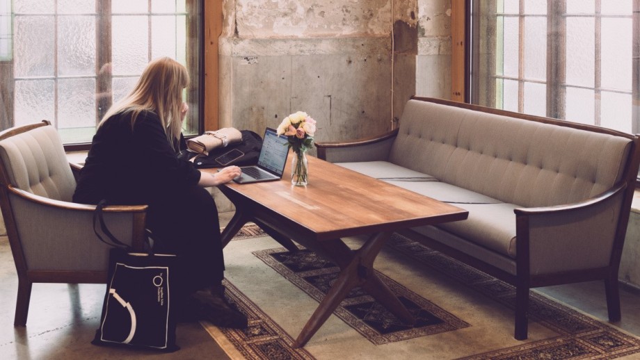 Student sitter i lenestol i rustikk rom og skriver på laptop.