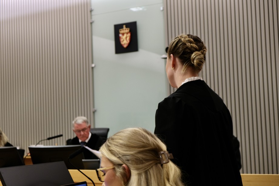 Kvinne i sort frakk står oppreist og snakker foran en dommer i en rettsal