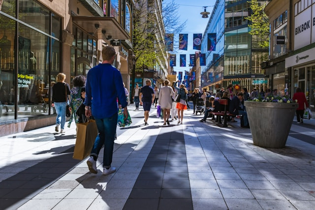 Foto av en gågate med butikker. Mennesker med bæreposer i hendene går nedover gaten med ryggen til kamera.