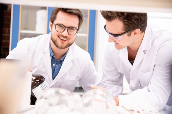 To unge menn i hvite labfrakker er på et laboratorium